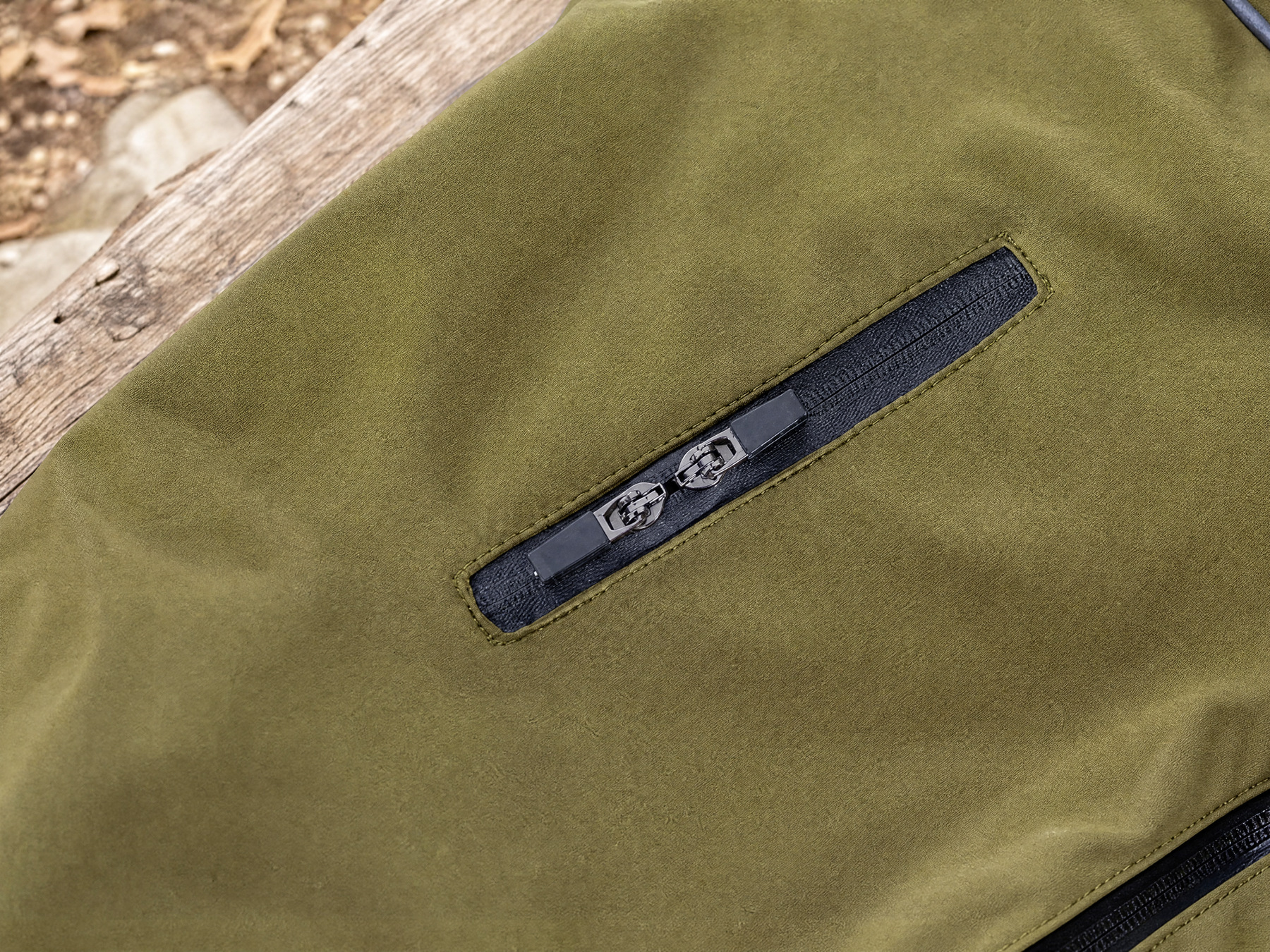 The green suit’s narrow back access slit is shown close up against a wooden trailhead bench.